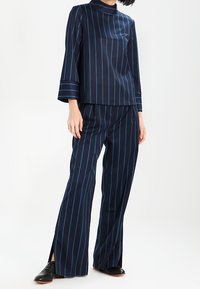 Completo a righe blu navy composto da un top maniche lunghe con collo alto e pantaloni larghi con fessure laterali.