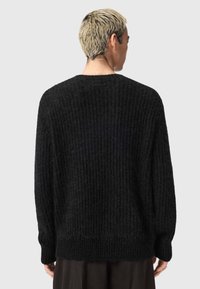 Chunky zwarte gebreide trui met ribbeltextuur, verlaagde schouders en een relaxte pasvorm. Heeft een brede halslijn en lange mouwen.