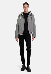 Grijze, lichte jas met een capuchon, elastische manchetten en een voorkleur. Gestyled met een zwarte trui en donkere broeken, met een gladde textuur.