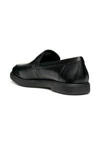 Mocassin en cuir noir à enfiler avec bout arrondi, couture minimaliste et semelle en caoutchouc noir, vu d'un angle faible à l'arrière.