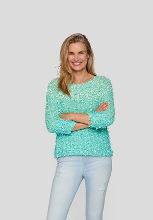 Light blue, textured sweater with a loose fit and round neckline. Features long sleeves and frayed fabric accents, paired with light jeans.