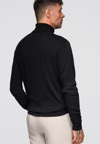 Czarny sweter z golfem o dopasowanym kroju, wykonany z miękkiego materiału. Posiada prążkowane mankiety i kołnierz, pokazany z tyłu.