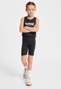 Svart atletisk tvådelad outfit bestående av en ärmlös topp med vit logotyp och åtsittande shorts. Bärs med grå och krämfärgade sneakers.