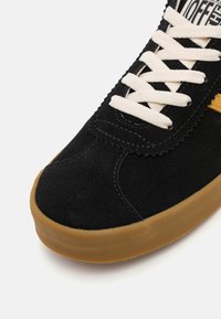 Zapatillas de ante negro con cordones beige y suela de goma. Presenta una parte superior texturizada y acentos cosidos a lo largo del borde.