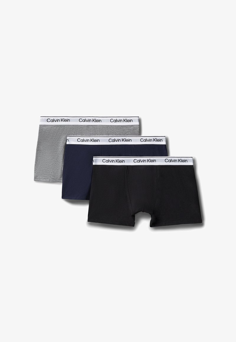 Trois paires de boxers pour hommes Calvin Klein en noir, bleu marine et gris avec des ceintures élastiques blanches affichant le nom de la marque.