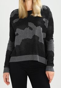 Černý a šedý svetr s maskáčovým vzorem, s žebrovanými manžetami a lemem, vyrobený z texturovaného materiálu, volný střih, rukávy délky do poloviny paže.