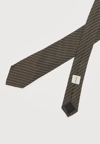 Καφέ γραβάτα με διαγώνιες λευκές ρίγες απλωμένη επίπεδα, εμφανίζοντας την ετικέτα της μάρκας Calvin Klein ραμμένη στην κάτω πλευρά.