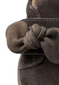 Bota de ante marrón con un detalle anudado en la correa. Textura suave, forma redondeada y costuras contrastantes en la parte superior.