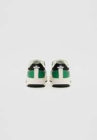 Grønne og svarte sneakers med en hvit hæltab, med kremfargede såler og svarte detaljer. Glatt materiale med kontrasterende teksturer.