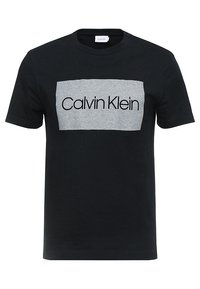 Camiseta negra de algodón con un diseño ajustado. Presenta un panel rectangular gris, con el texto "Calvin Klein" en negrita y en color negro.