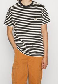 T-shirt rayé noir et crème en coton, comportant une poche poitrine avec une étiquette logo carrée et un col ribcage.