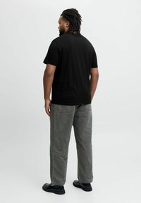 Sort bomulds t-shirt med korte ærmer, parret med grå vide bukser og sort fodtøj, set bagfra mod en lys baggrund.