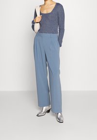 Haut à manches longues en maille bleu foncé, associé à un pantalon large bleu clair. Des bottines argentées à la cheville ajoutent un contraste avec une finition métallique.