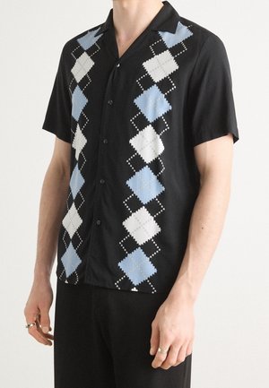 Homme portant une chemise noire à manches courtes avec des motifs losanges argyle bleus et blancs à l'avant.
