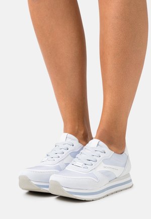 Des chaussures de sport blanches in combinant des matériaux lisses et texturés, avec des lacets, des accents bleus subtils et un design de semelle superposée.