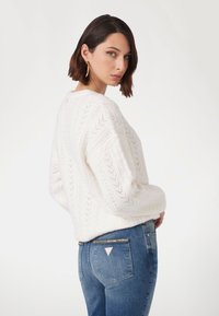 Witte gebreide trui met een chevronpatroon, gecombineerd met blauwe jeans met een decoratieve accent op de achterzak.