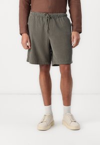 Pantalones cortos de pana verde oliva con cinturilla elástica y cordón. Presentan bolsillos laterales y un corte relajado. Combinados con zapatillas beige.