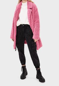 Rosa fluffig oversized kappa, vit ribbad topp, svarta cargo-byxor med fickor och svarta snörade klumpiga stövlar. Mjuk textur genomgående.