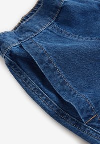 Tissu en denim bleu avec des coutures détaillées et une ceinture élastique, montrant une section froncée et pliée.