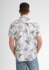 Camisa de manga corta de tejido ligero con un patrón floral que presenta flores azules y hojas de palma verdes sobre un fondo claro.
