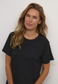 Camiseta negra de manga corta con un cuello redondo, fabricada en tejido suave. Presenta un corte holgado y una textura lisa.