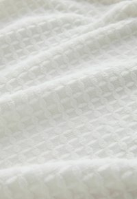 Balts faktūrēts audums ar rūtainu rakstu, ar maigu, austu virsmu, kas izskatās viegls un elpojošs.