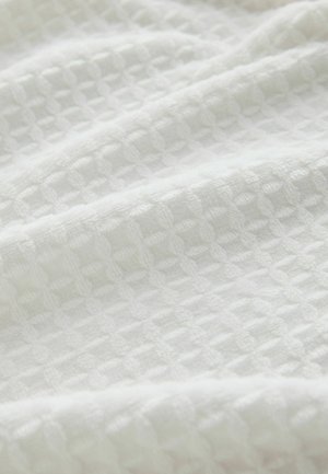 Balta tekstūruota audinys su langelių raštu, pasižymintis minkštu, austiniu paviršiumi, kuris atrodo lengvas ir orui laidus.