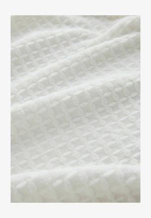 Balta tekstūruota audinys su langelių raštu, pasižymintis minkštu, austiniu paviršiumi, kuris atrodo lengvas ir orui laidus.