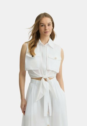 Camicia bianca a maniche corte, con bottoni e due tasche sul petto, con un nodo davanti. Abbinata a una gonna bianca legata in vita.