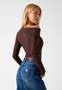 Top marrone a maniche lunghe con scollo a barca abbinato a jeans blu a vita alta con una toppa a triangolo sulla tasca posteriore. Tessuto liscio e aderente.