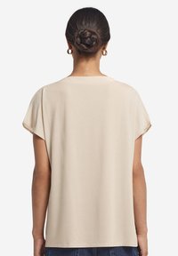 Beżowy top z krótkim rękawem o luźnym kroju, okrągłym dekolcie i miękkiej tkaninie, z lekko zwężającymi się bokami i gładkim, nieozdobionym tyłem.