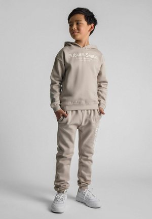 Beige sweatshirt en joggers set met de tekst "Future Skate", gemaakt van zachte stof, met geribde manchetten en witte sneakers.