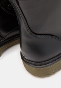 Czarne skórzane buty z gładkim wykończeniem, detalami stębnowania i teksturowaną brązową gumową podeszwą. Widok z boku, ze szczególnym uwzględnieniem pięty.
