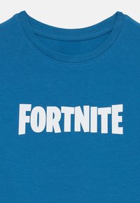 Mėlynas medvilninis marškinėliai su dideliu baltu "FORTNITE" logotipu. Apvalia iškirpte, trumpomis rankovėmis, lygi tekstūra ir vienodais siūlais.