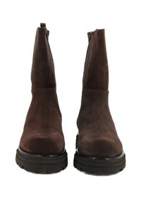 Un paio di stivali alla caviglia in suede marrone scuro con suole nere spesse, pannelli laterali elasticizzati e linguette sul retro.