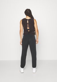 Top nero senza maniche con un dettaglio a nodo sul retro e accenti a taglio, abbinato a pantaloni neri e sneakers bianche. Tessuto con una texture liscia.