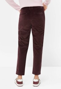 Bordeaux Cord-Jeans mit geradem Schnitt, ausgestattet mit Gesäßtaschen und einem umgeschlagenen Saum, kombiniert mit weißen und bordeauxfarbenen Sneakers.