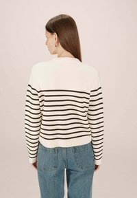 Pull en tricot crème avec des rayures brun foncé, doté d'un col, de manches longues et d'un ourlet droit. Assorti à un denim bleu clair.