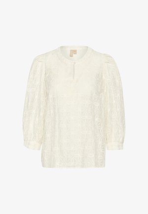 Blusa crema con collo rotondo e dettaglio a chiave, caratterizzata da motivi floreali in rilievo e maniche a palloncino. Tessuto morbido con una leggera lucentezza.