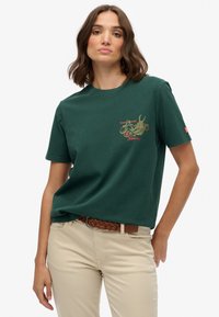 Groen katoenen T-shirt met een goudrode draakafbeelding op de borst. Het heeft een ronde hals en korte mouwen.