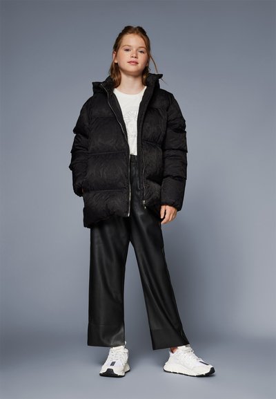 Black padded jacket with a textured pattern, featuring a high collar and zipper. Paired with wide black leather pants and white sneakers.