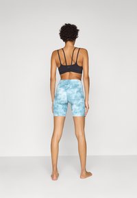 Black sports bra with multiple thin straps paired with light blue tie-dye high-waisted shorts. Smooth texture and fitted shape.