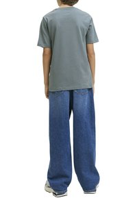 Camiseta de algodón gris con mangas cortas, combinada con unos vaqueros de mezclilla azul, amplios y holgados. Detalles notables incluyen los bolsillos traseros en los vaqueros.