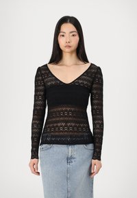 Top lungo nero in pizzo con scollatura a V. Il tessuto presenta motivi floreali e sezioni trasparenti, abbinato a una silhouette aderente.