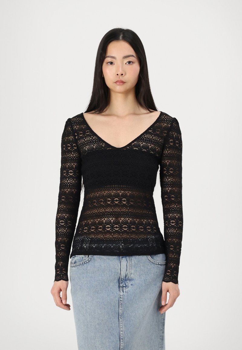 Top lungo nero in pizzo con scollatura a V. Il tessuto presenta motivi floreali e sezioni trasparenti, abbinato a una silhouette aderente.