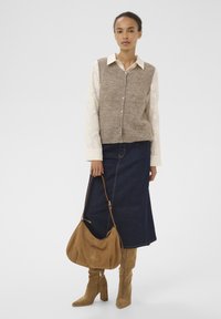 Strikket beige vest over en hvid blomstret langærmet skjorte, parret med en denimnederdel og beige ruskindsankle støvler. Holder en brun taske.