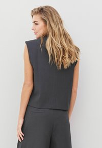 Top fără mâneci de culoare gri închis, cu un croi ajustat, textură netedă și design minimalist. Vederea din spate arată o lungime ușor scurtă.