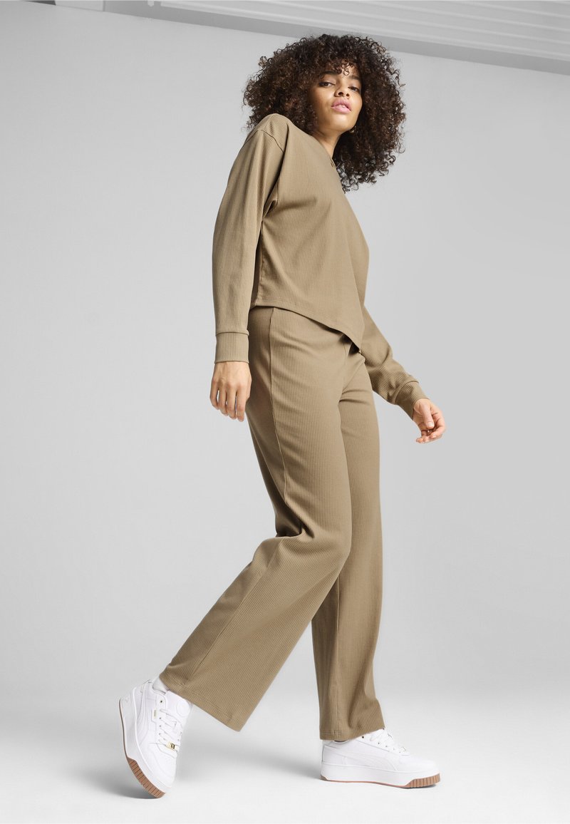 Set de loungewear cu model în carouri, de culoare khaki, format dintr-un top cu mâneci lungi, cu o croială lejeră, și pantaloni cu croielă largă, asortați cu adidași albi și un material texturat.
