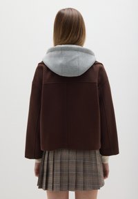 Chaqueta marrón con capucha gris, con un diseño cuadrado y mangas set-in. Combinada con una falda de cuadros plisada en tonos marrones y grises.