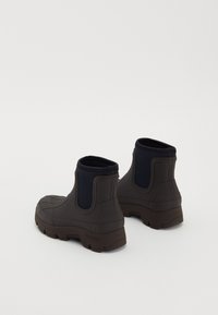 Botas de tobillo impermeables de color marrón oscuro con suela de goma texturizada y acentos de tela azul marino alrededor del cuello. Diseño elegante y moderno.